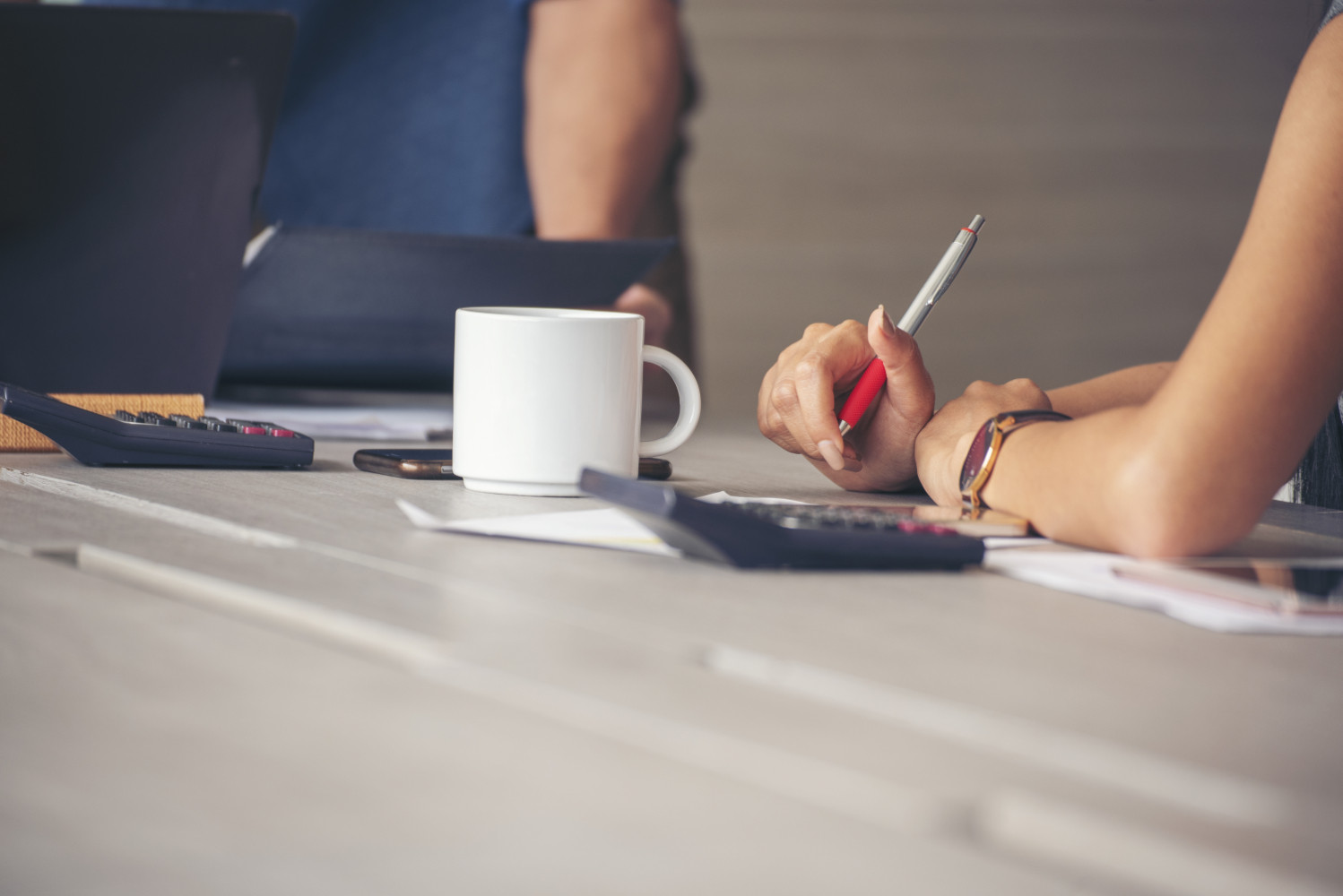 Una mesa de oficina con café y el brazo de una trabajadora